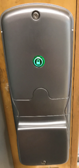 Internal view of metal door lock with rubber door lock button that is lit green signifying door has unlocked, attached to wooden door