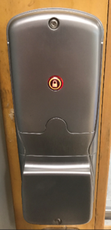 Internal view of metal door lock with rubber door lock button that is lit red signifying door is locked, attached to wooden door